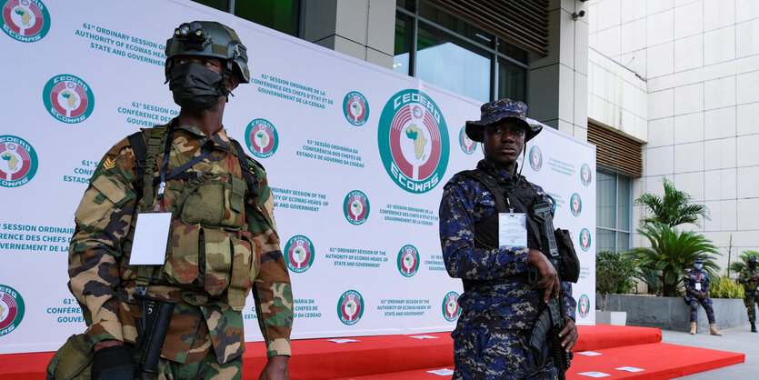 Zwei Soldaten stehen vor einer Plakatwand zu Ecowas