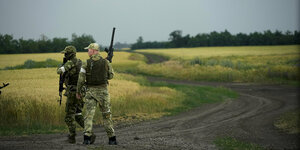 Zwei bewaffnete Männer in Militäruniform stehen in einem dunkelgelben Weizenfeld
