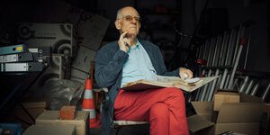 Ein alter Mann in seiner Garage, er trägt eine rote Hose und blättert in einem Aktenordner