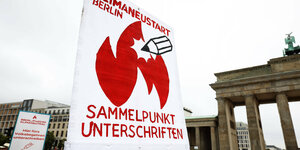 Ein Plakat ruft für Unterschriften für Klimaneustart Berlin auf, im Hintergrund das Brandenburger Tor