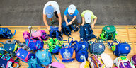 Drei Kinder stellen in einer Grundschule auf einem Podest ihre Schultaschen ab