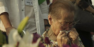 ältere Frau, die sich weinend ein Taschentuch vor den Mund hält