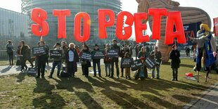 STOP CETA rote Buchstaben werden vor dem Eu Parlament in Strassburg hochgehalten, ein hölzernes trojanisches Pferd ist dahinter zu sehen