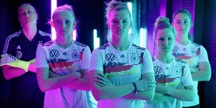 Fünf Frauen in den Triktots der Fußballnationalmannschaft, die Arme verschränkt.