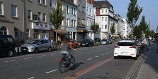 Eine Radfahrerin fährt auf einer schmalen Fahrradspur neben parkenden Autos