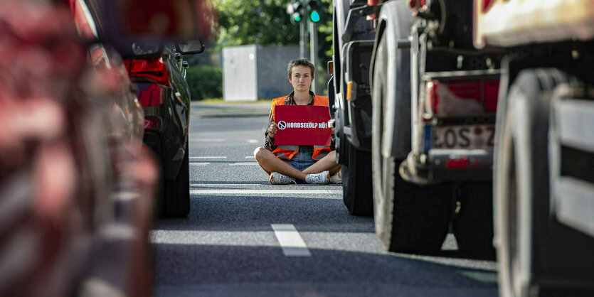 Eine Person mit einem Schild sitzt zwischen Fahrzeugen auf einer Straße