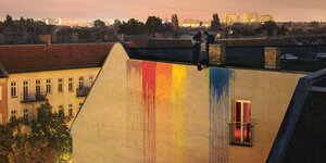 Regenbogenfarben an einer Brandmauer. Auf dem Dach ist eine Person zu erkennen