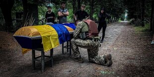 Ein Soldat kniet vor einem mit der ukrainischen Flagge bedeckten Sarg