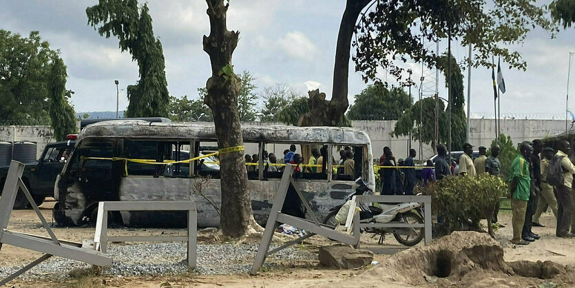 Ein ausgebrannter Bus steht vor einem Gefängnis