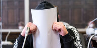 Ein Mann in einem Gerichtssaal hält sich ein Papier vors Gesicht
