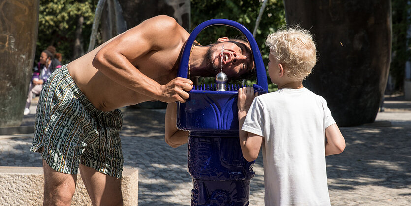 Ein Mann trinkt aus einem bleuen Trinkbrunnen