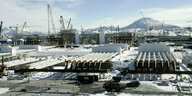 Fabrikanlagen - lange Rohre und Kräne im Schnee, im Hintergrund ein Berg