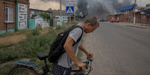Ein Mann überquert mit einem Fahrrad eine Straße, dahinter Rauchschwaden
