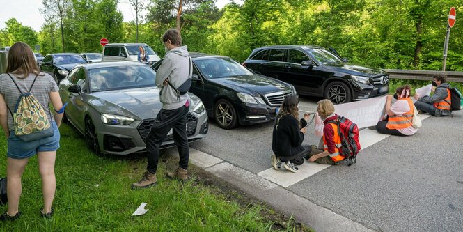 Klimaaktivisten sitzen auf einer Straße, davor eine Autoreihe