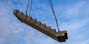 Eine Treppe hängt an Stahlseilen in der Luft vor bewölktem Himmel