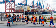 Hafenarbeiter gehen vor einem Containerschiff entlang