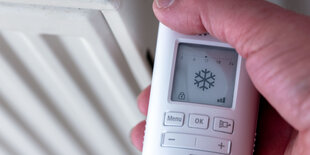 Hand an Heizungsthermostat mit Eiskristall-Symbol