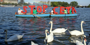 2 Boote mit STOP CETA roten Buchstaben, die von Aktivisten gehalten werden, davor Schwäne auf der Binnenalster