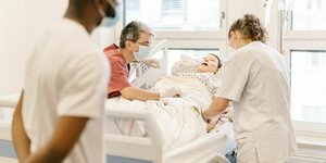 Drei Personen beugen sich in dem simulierten Krankenhauszimmer des Skills- und Simulationszentrum der Hochschule Bremen über eine lebensgroße Patientenpuppe im Krankenbett