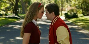 Die Schauspielerin Elle Fanning steht links, Gesicht an Gesicht mit Colton Ryan. Sie sind beide jung. Fanning trägt ein rotes Shirt und hat lange, blonde Haare. Ryan trägt eine College Jacke in Rot mit gelben Ärmeln. Er hat kurze dunkle Haare.