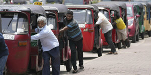 Männer schieben ihre kleinen TukTuk-Autos von draußen, mit einem Arm nach drinnen gestreckt, ans Lenkrad