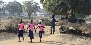 Drei Schülerinnen in rosafarbenen Schuluniformen und ein Polizist