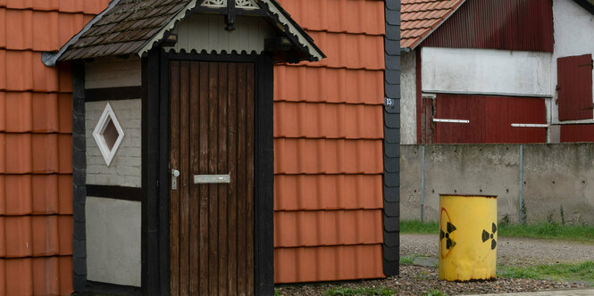 Ein Fass mit einem aufgemalten Atomzeichen steht neben einem Hauseingang