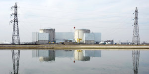 Atomanlage und zwei Masten einer Hochspannungsleitung spiegeln sich im Wasser