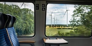 Blick durch ein Zugfenster auf eine Landschaft mit Windanlagen