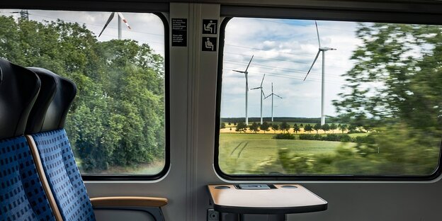 Blick durch ein Zugfenster auf eine Landschaft mit Windanlagen