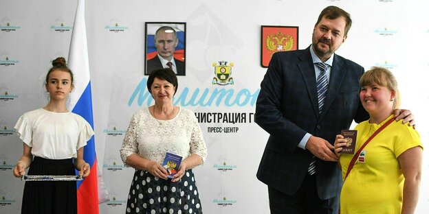 Zeremonie: Einer Frau in gelbem Kleid zeigt ihren russischen Pass, umringt von Beamten und im Hintergrund hängt Putin an der Wand