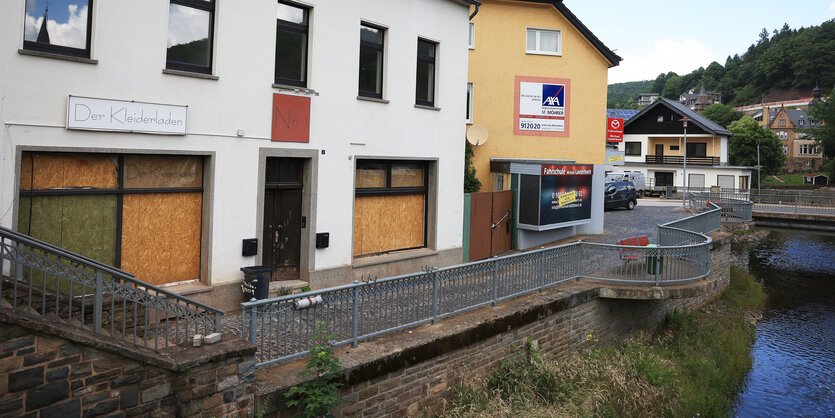 Die Fenster einer Straßenzeile sind mit brettern zugestellt, darunter ein kleiner Fluß