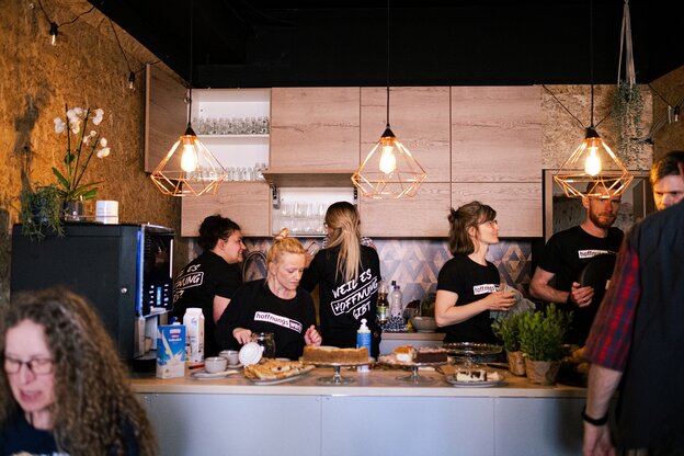 Um ein Kuchenbuffet stehen viele Leute in schwarzen Shirts und unterhalten sich angeregt Um ein Kuchenbuffet stehen viele Leute in schwarzen Shirts und unterhalten sich angeregt
