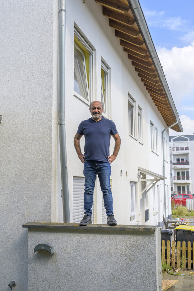 Ein Mann steht auf einer Mauer, dahinter ein weiß gestrichenes zweistöckiges Haus Ein Mann steht auf einer Mauer, dahinter ein weiß gestrichenes zweistöckiges Haus