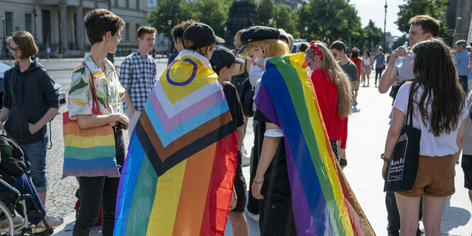 2 Menschen mit Umhängen aus Regenbogenfarben sind von hinten zu sehen in einer Gruppe