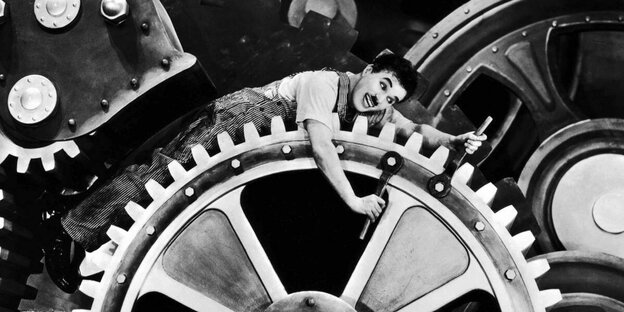 Charlie Chaplin in „Modern Times“ (1936) auf einem großen Zahnrad liegend