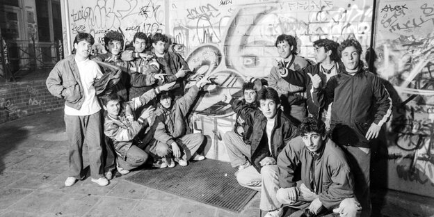 Auf einem schwarz-weiß Foto posiert eine Gruppe Jugendlicher vor einer Wand mit Grafiti, die Zahl "36" groß auf der Mauer