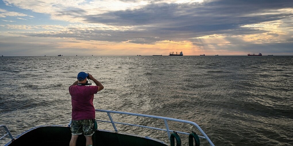 Ein mann steht auf einem Schiff und blickt über das Meer zum Horizont, wo weitere Schiffe zu sehen sind