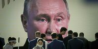Das Gesicht von Wladimir Putin ist auf einem riesigen Bildschirm zu shene, davor stehen einige Menschen