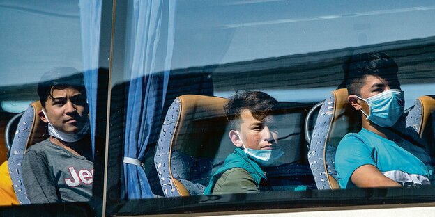 Drei ältere Jungen sitzen in einem Reisebus und gucken aus dem Fenster
