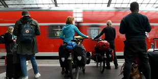 Menschen stehen an einem Bahnsteig, zwei haben Fahrräder dabei, und warten auf einen Regionalzug