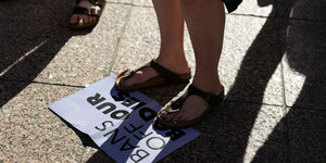 Jemand steht mit den Füssen auf einem Protestplaktat auf dem zu lesen ist " BANS OF OUR BODIES"
