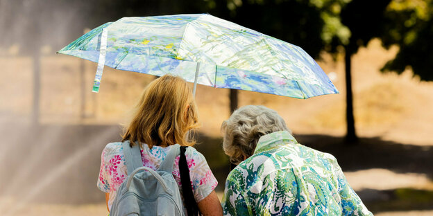 Zwei Frauen schützen sich mit einem Regenschirm vor der Sonne