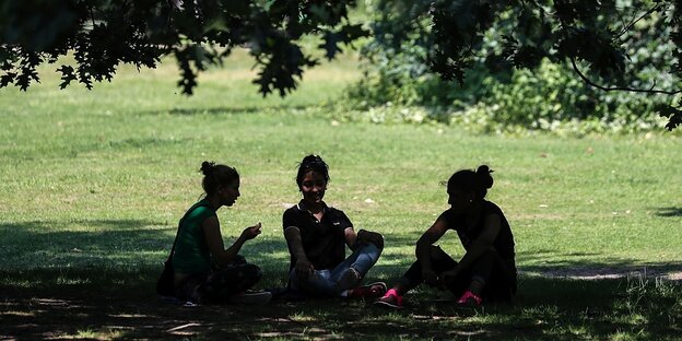 Drei Frauen sitzen unter einem Baum im Schatten