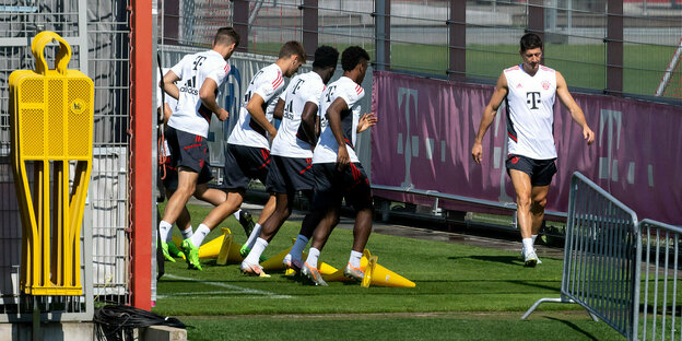 Mehrere Bayernspieler trainieren auf dem Fußballplatz, etwas losgelöst von ihnen geht Robert Lewandowski