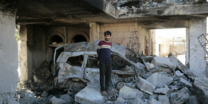 Ein Mann steht auf und zwischen Trümmern vor einem ebenfalls zerstörten Auto.
