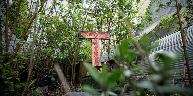 Ein beschädigtes Friedhofskreuz mit der Aufschrift ·unvergessen· steht in einer Häuserlücke