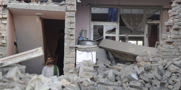 Zwei Männer schauen aus der zertrümmerten Wand eines Wohnhauses
