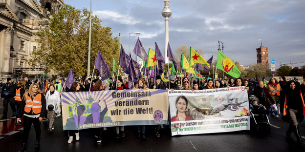 Eine Demo läuft mit dem Transparent "Women defend Rojava" im Hintergrund ist der Berliner Fernsehturm