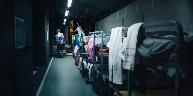 Mehrere, mit Kleidungsstücken behangene Stockbetten stehen hintereinander in einem schmalen Raum
